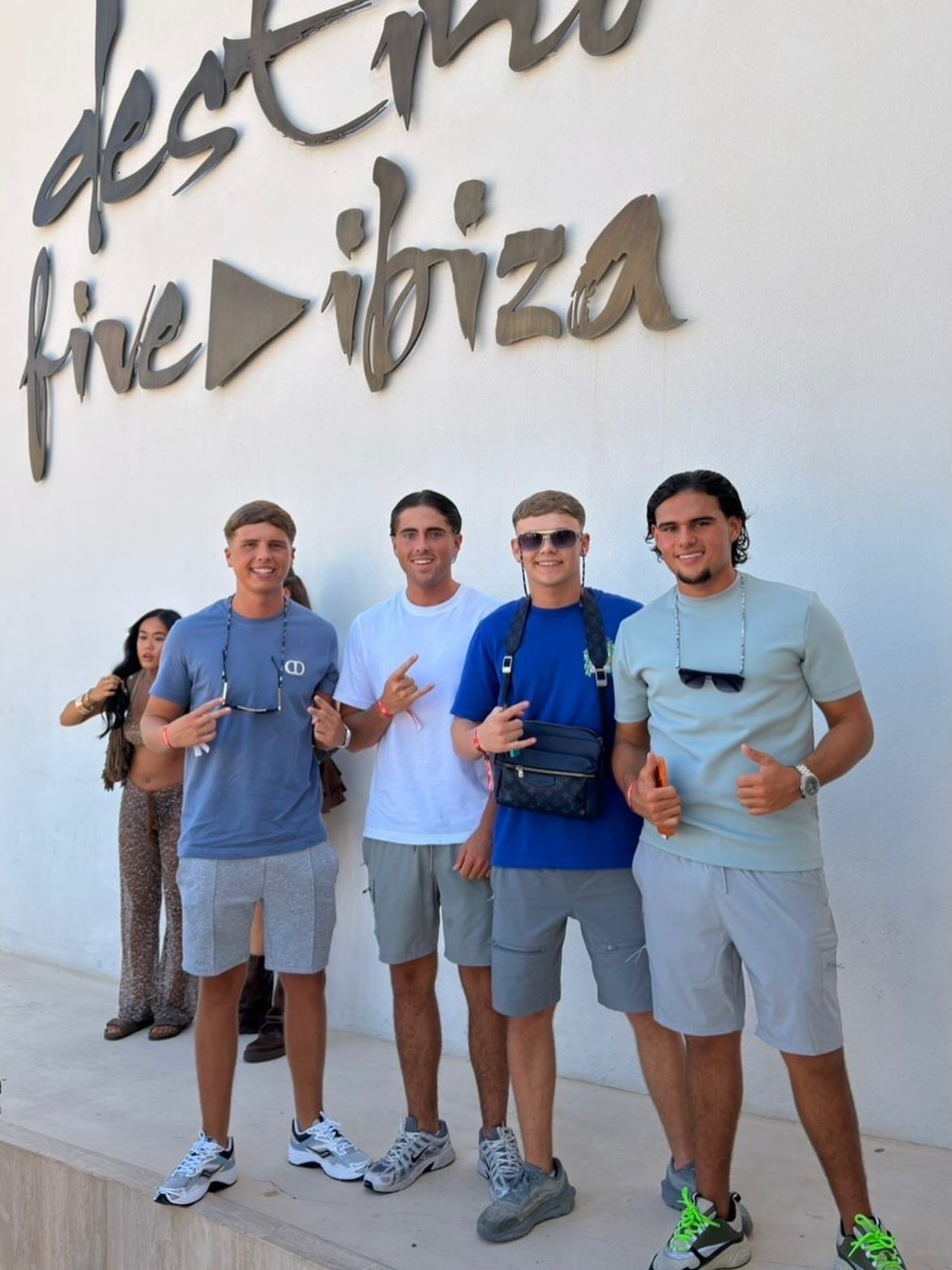 Four men posing in casual summer outfits and shorts in front of a white wall.