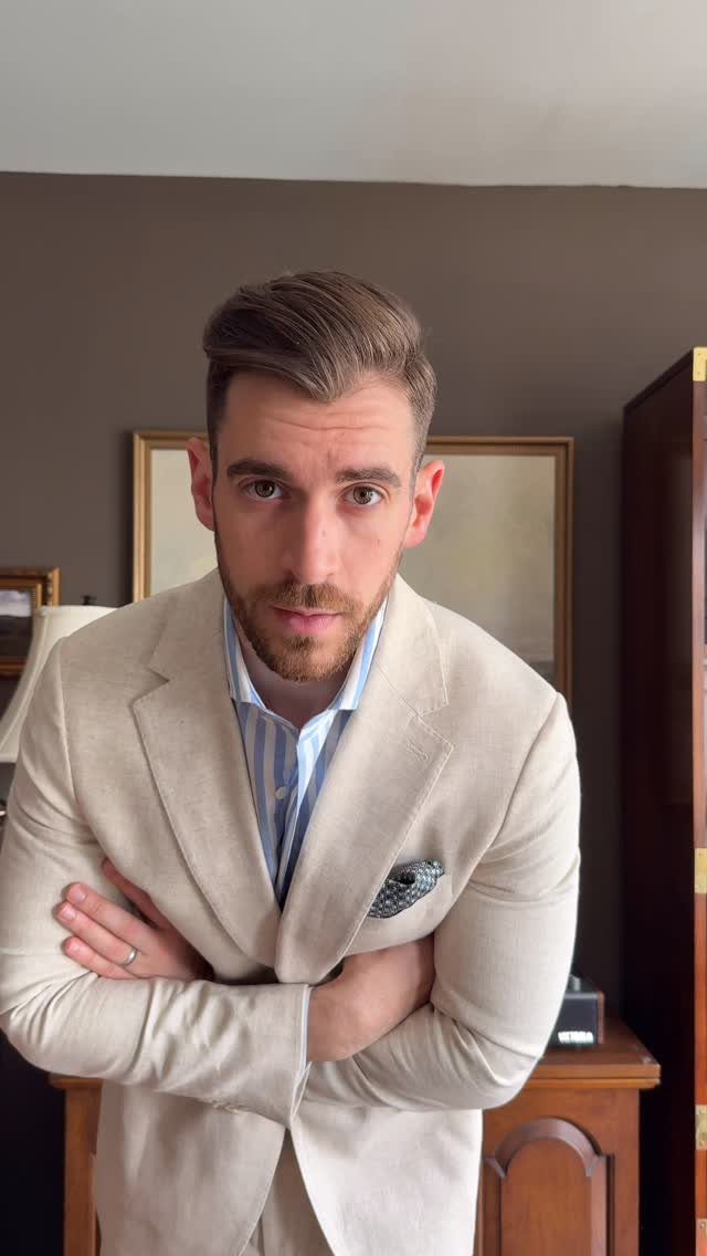 Man with a beard wearing a light beige linen suit jacket and striped shirt.