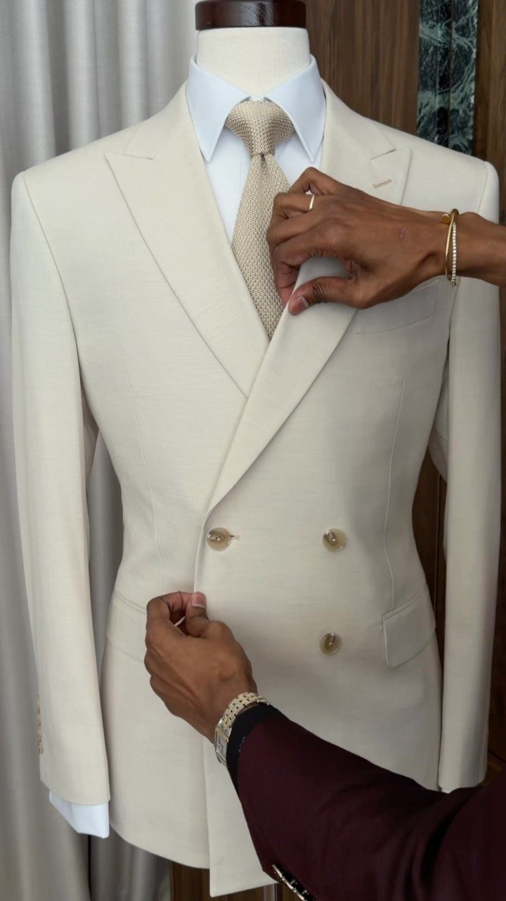 Cream double-breasted suit jacket on a mannequin being adjusted by hands.