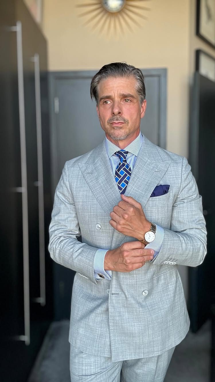Man in a light grey double-breasted patterned suit adjusting his cuff.