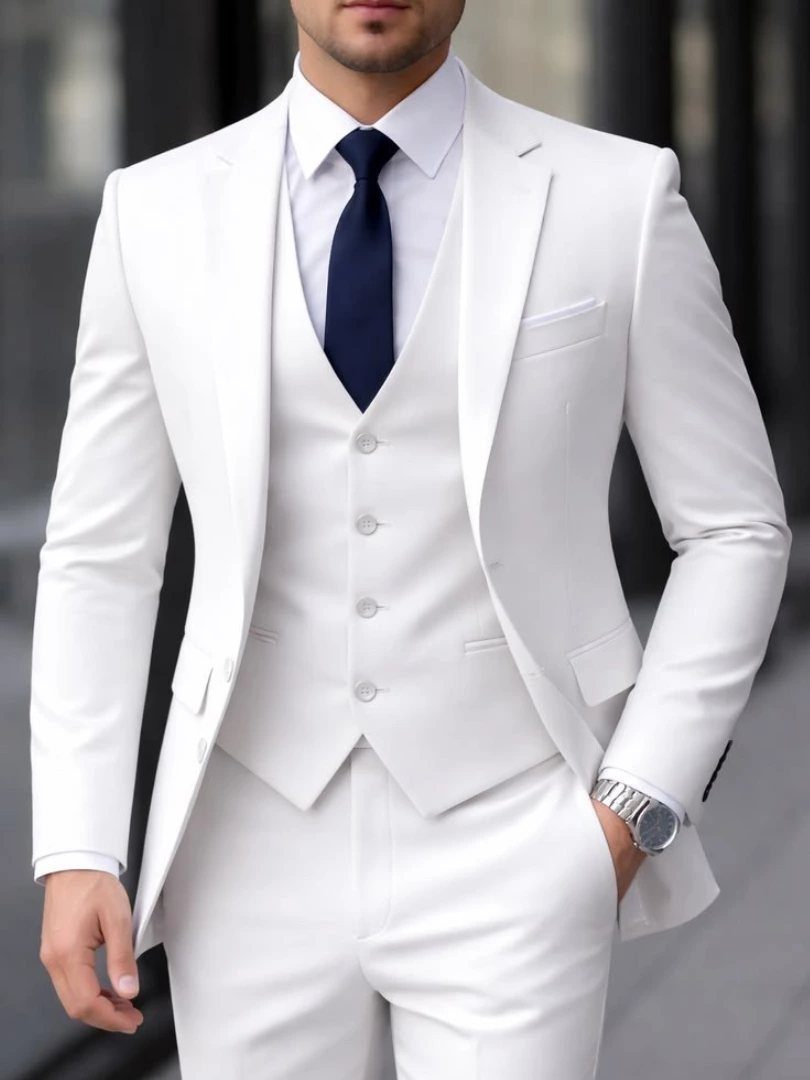Man wearing a formal white three-piece suit with a navy blue tie and silver watch.