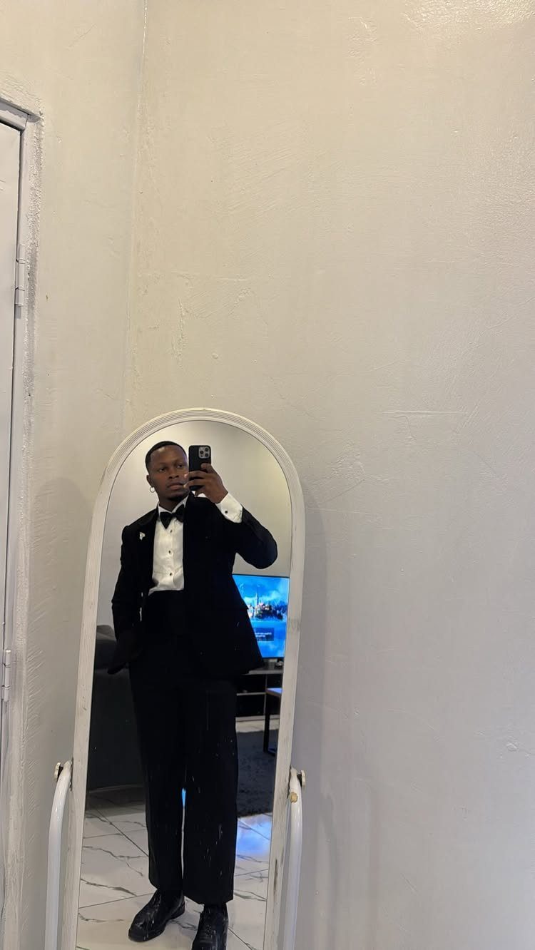 A man posing in a mirror wearing a classic black tuxedo and bow tie.