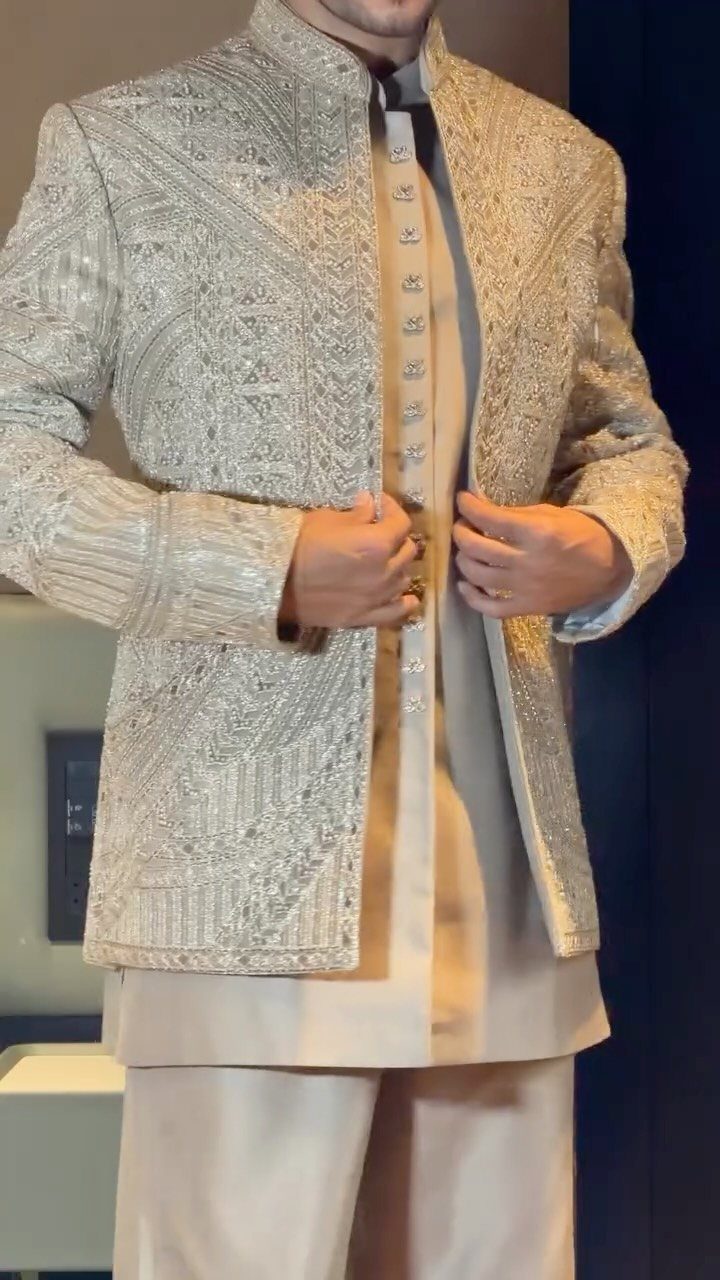 Man wearing an intricately embroidered cream-colored jacket sherwani with matching traditional attire.