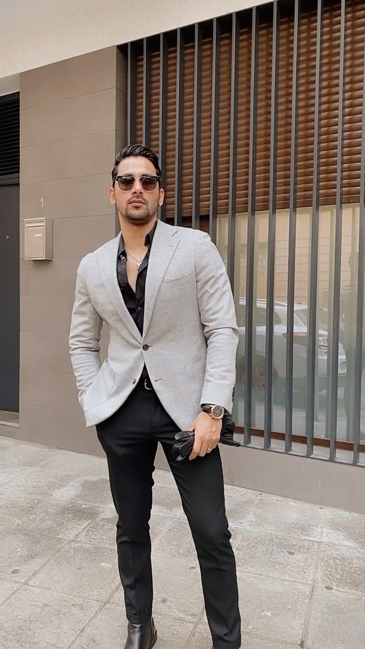 Man in a light grey blazer, black shirt, and black trousers posing outdoors.