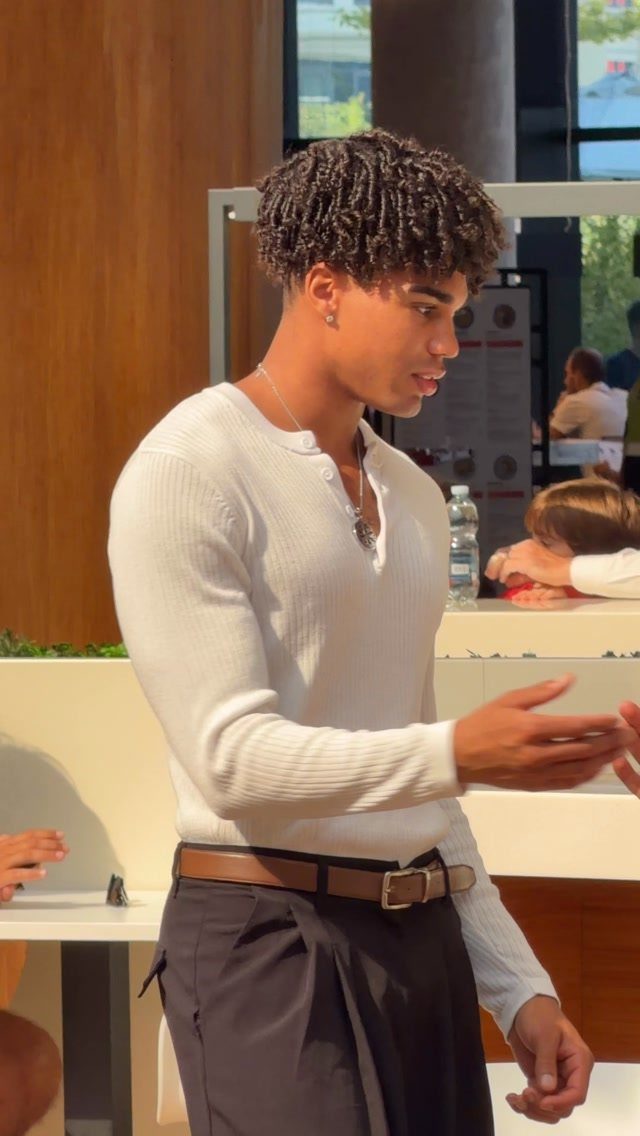 A young man in a white long-sleeve ribbed Henley shirt and dark pants.
