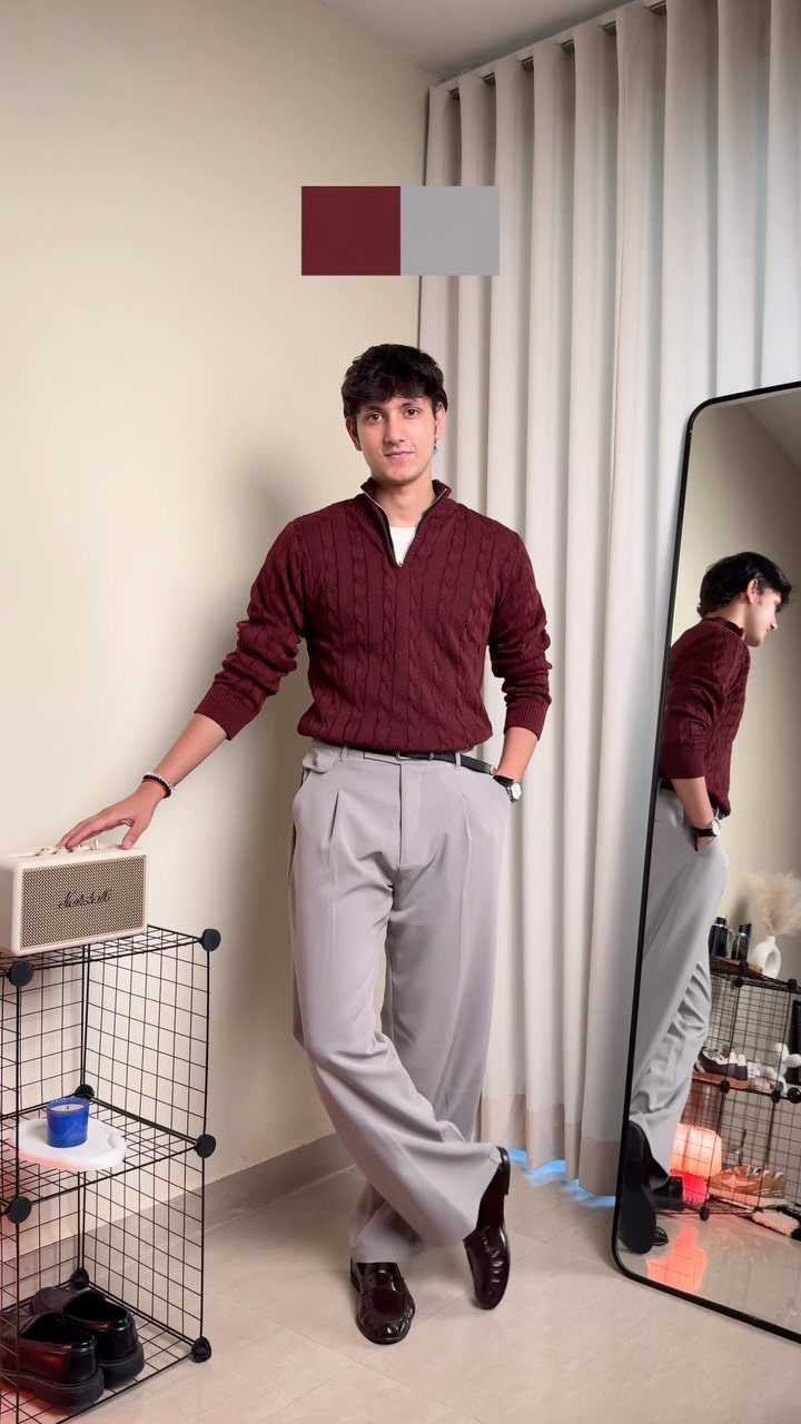 Man wearing a maroon cable-knit sweater and grey tailored trousers standing in a room.