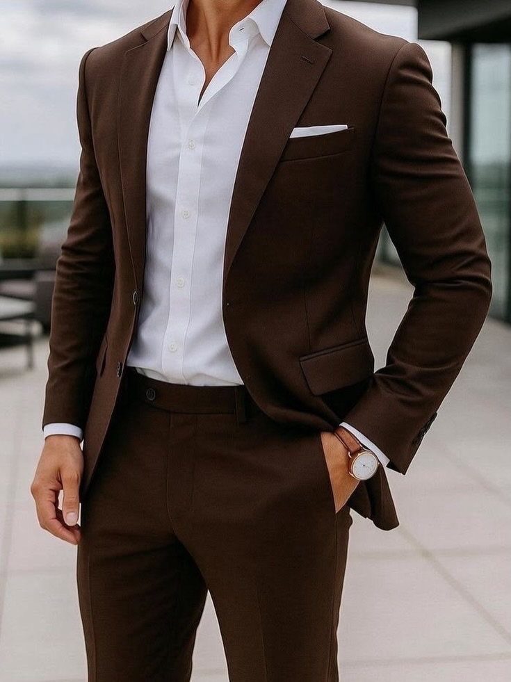 Man in a tailored dark brown suit and white shirt standing outdoors.