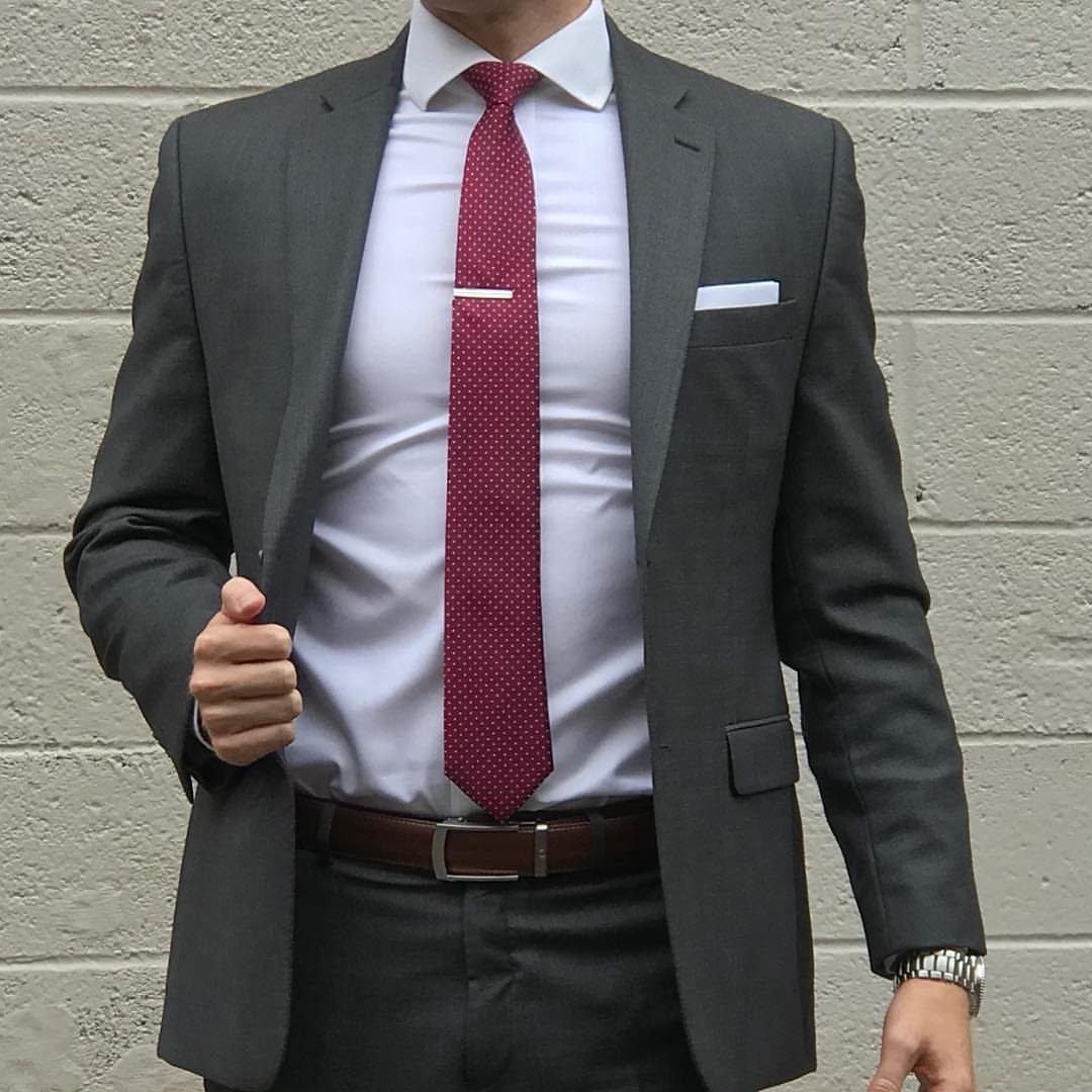 Man in a grey suit wearing a maroon tie, silver tie clip, and brown leather belt.
