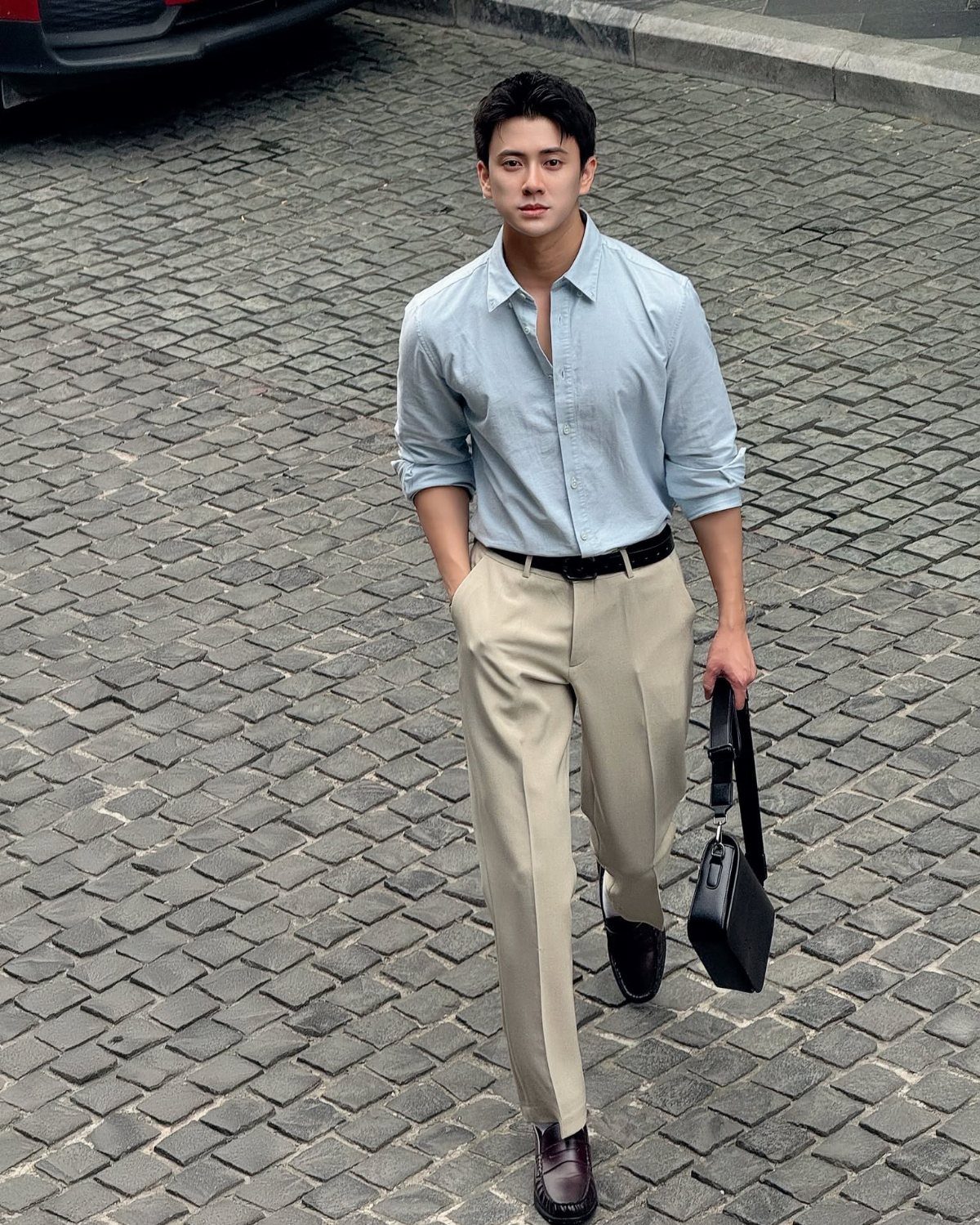 A man in a light blue shirt and beige trousers walks across a cobblestone street.
