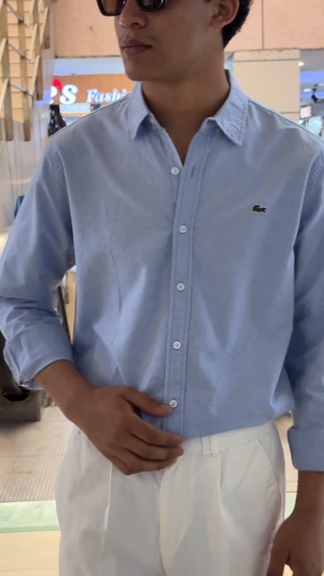 Man in a light blue button-down shirt and white trousers wearing dark sunglasses.