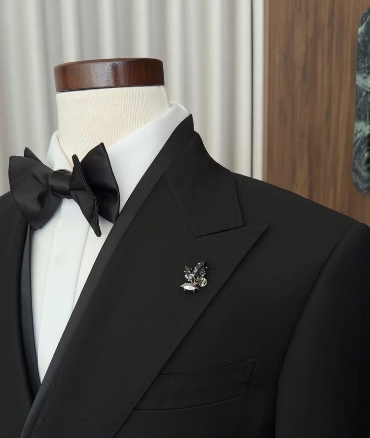 A black tuxedo jacket with a white shirt, black bow tie, and silver lapel pin.