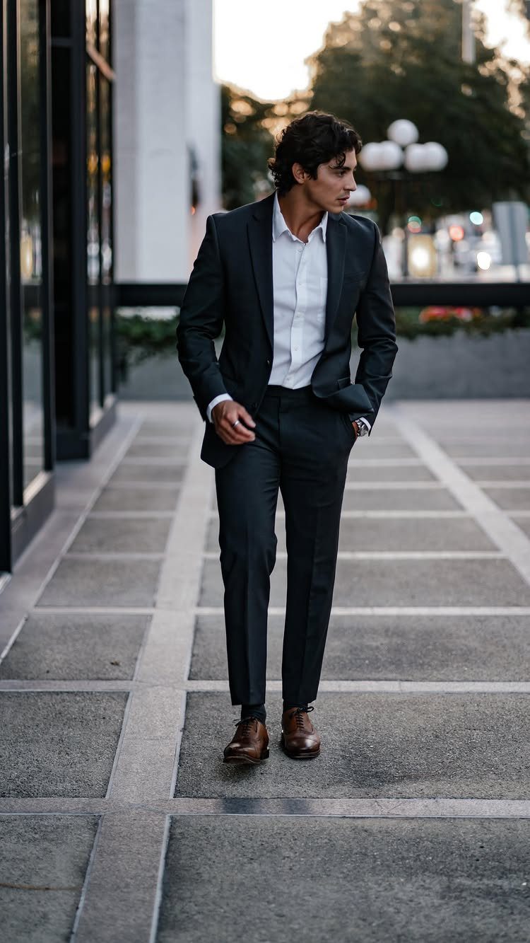 A man in a dark suit and white shirt walking on a city sidewalk.