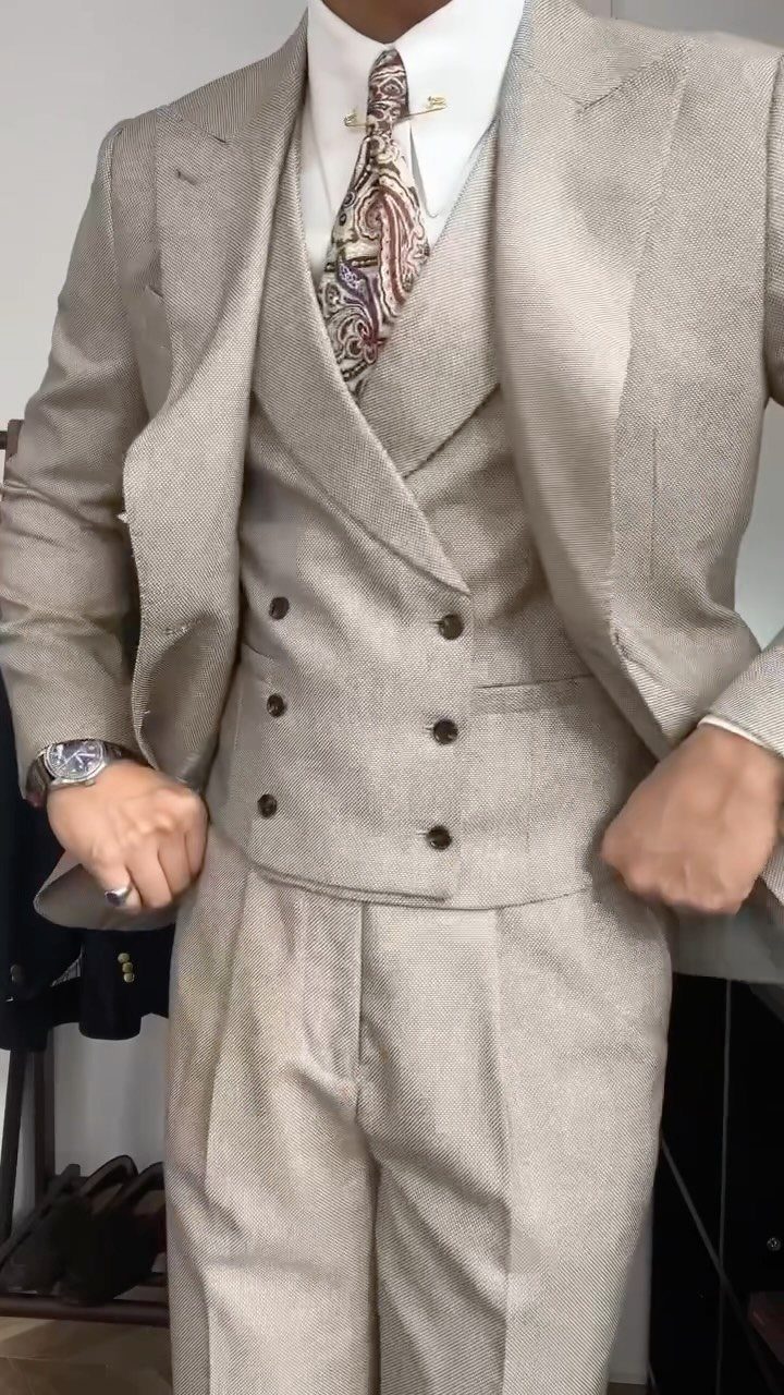 A man wearing a light beige three-piece textured suit with a paisley tie.