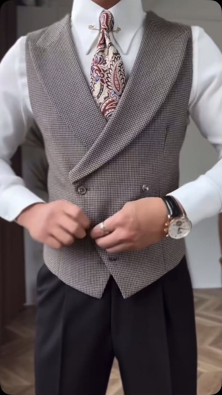 A man in a white shirt, paisley tie, and grey double-breasted waistcoat adjusting his clothing.