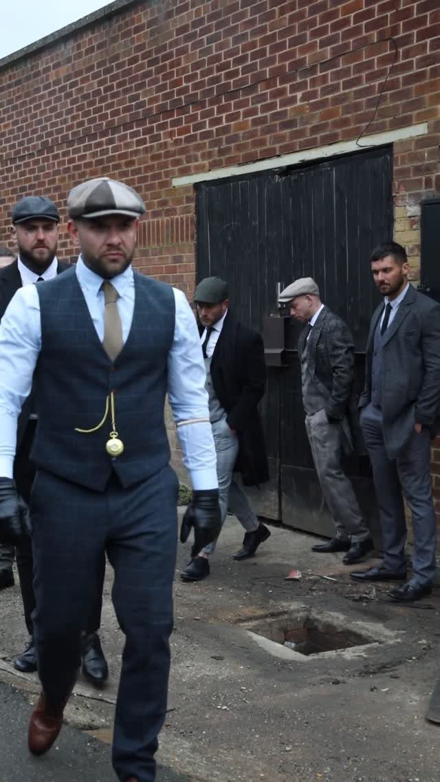 Men wearing 1920s style waistcoats and flat caps walking outdoors.