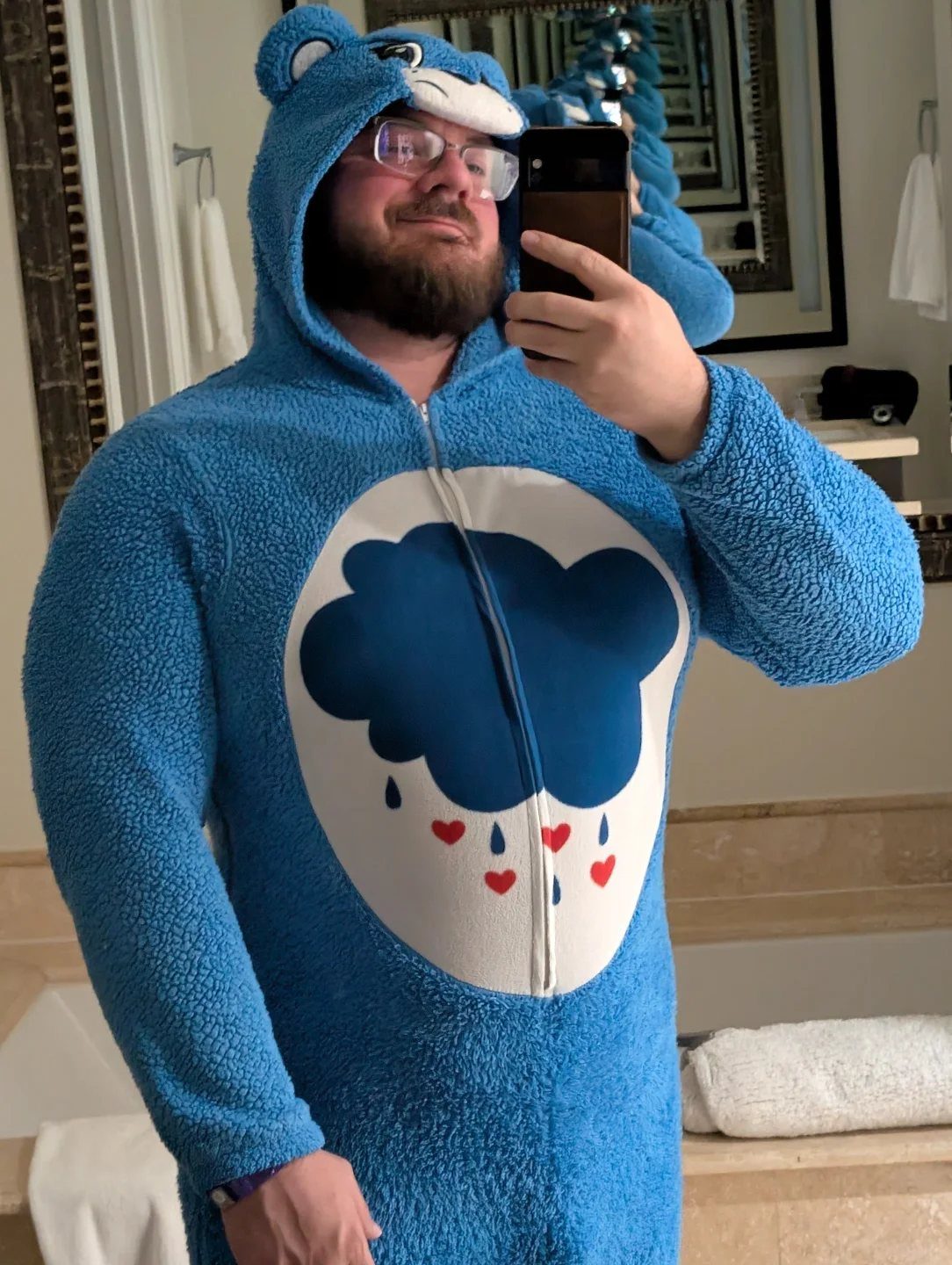 Man in a blue Grumpy Bear hooded onesie taking a mirror selfie.