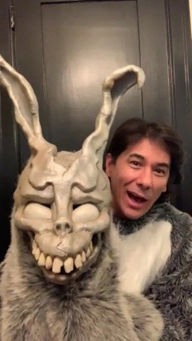 A man smiling next to a large, creepy grey and white furry bunny mask.