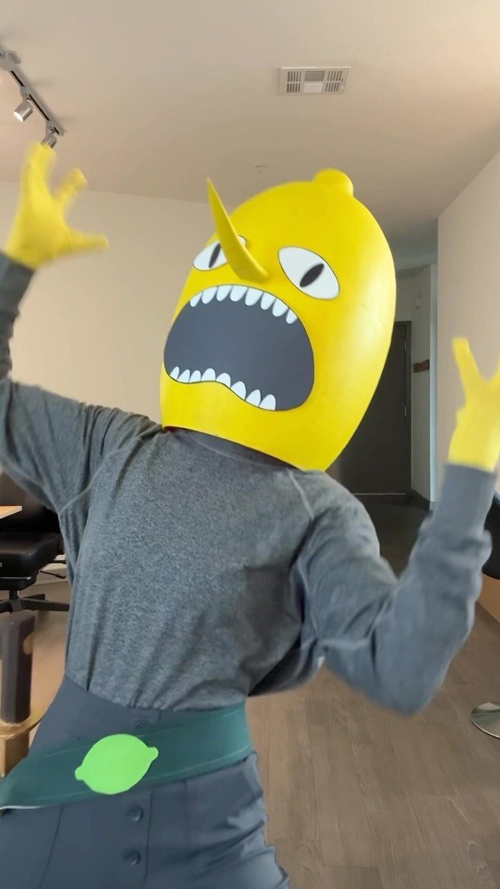 A person wearing a large yellow lemon mask and yellow gloves while posing.
