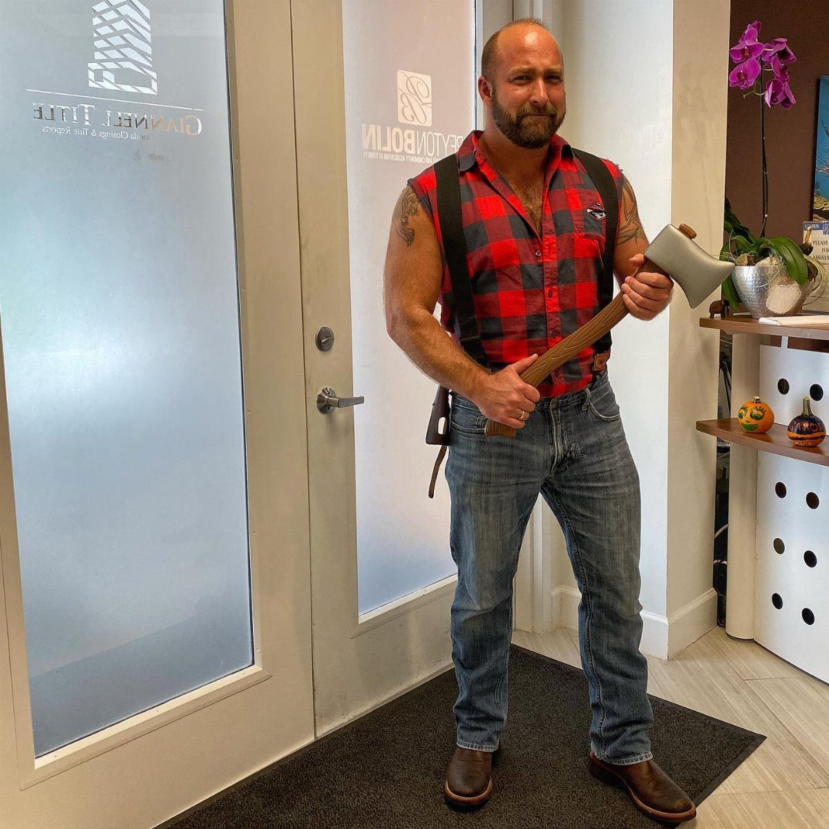 A man in a red plaid shirt and jeans holding a prop axe.
