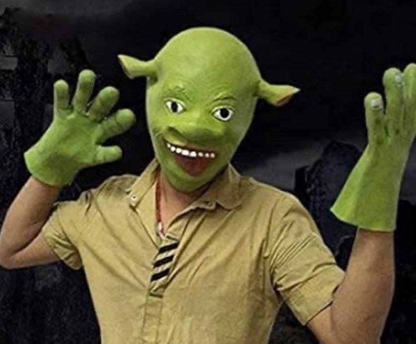 Man in a green Shrek mask and tan shirt posing with hands raised.