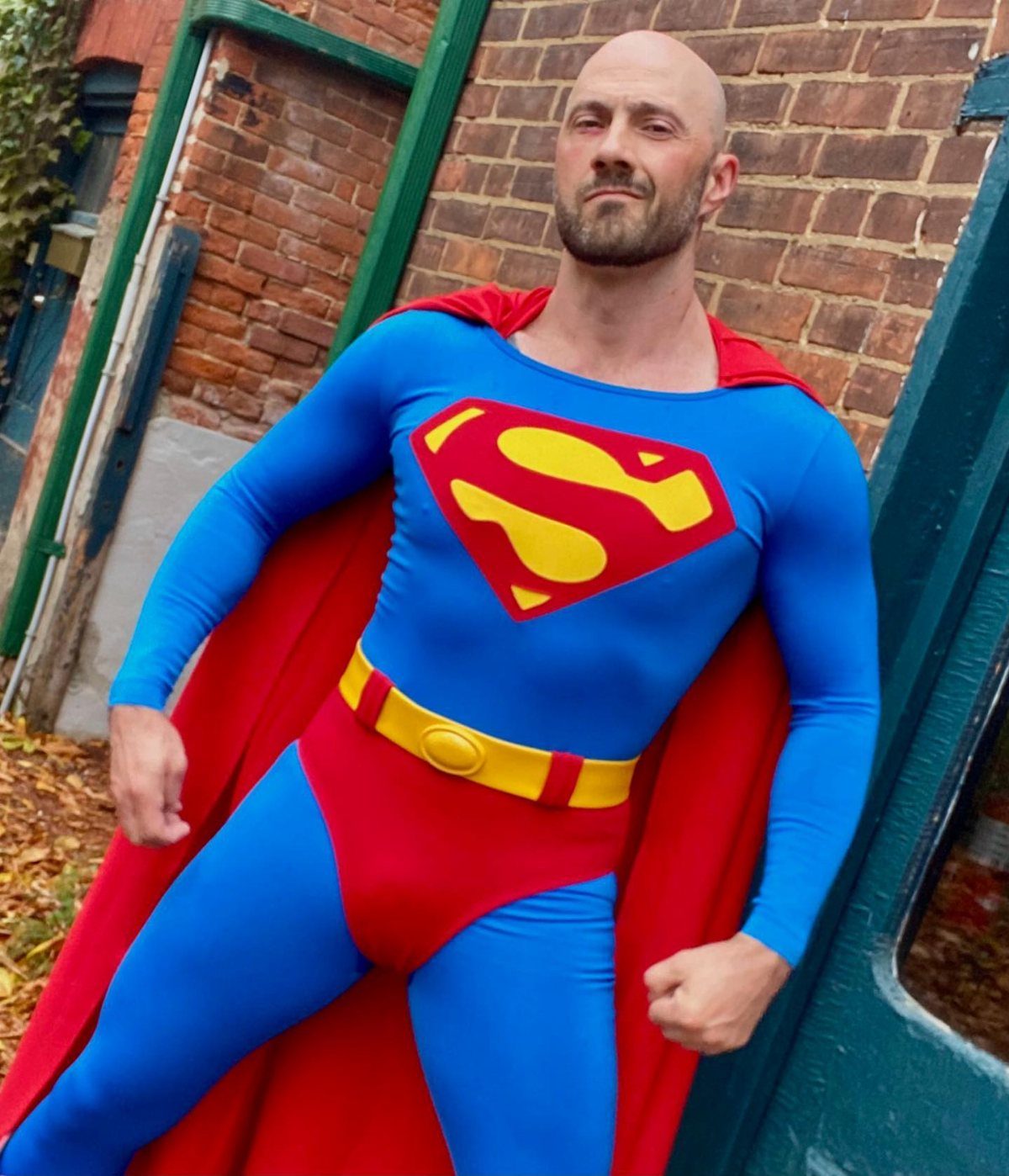 A man posing in a blue and red Superman superhero costume with a red cape.