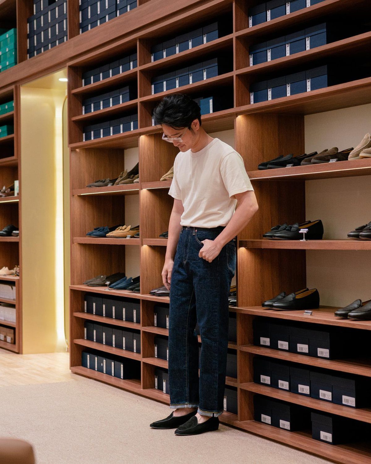 A man wearing dark blue denim jeans and a white t-shirt in a shoe store.