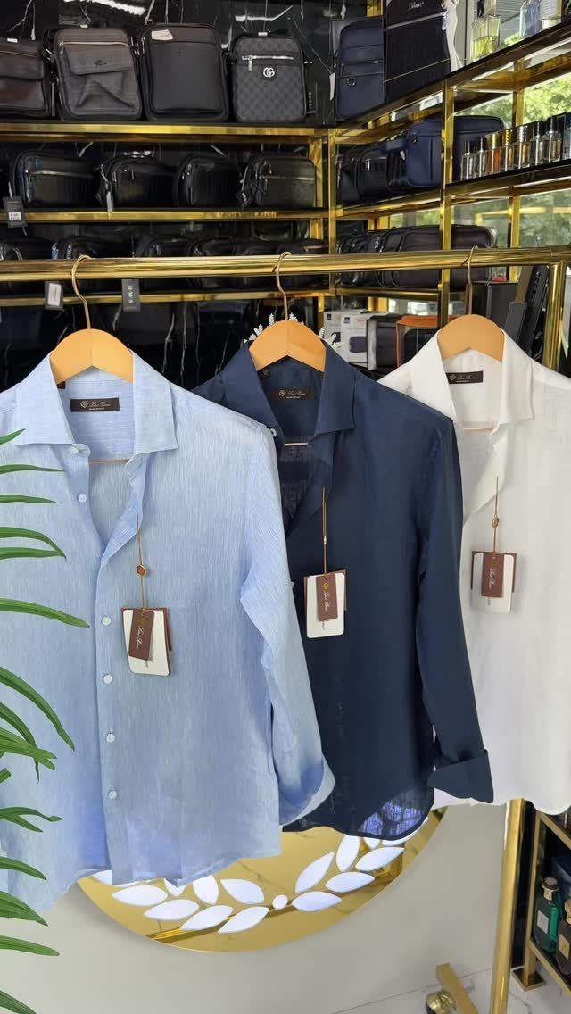 Three button-down shirts in blue, navy, and white hanging on a gold clothing rack.