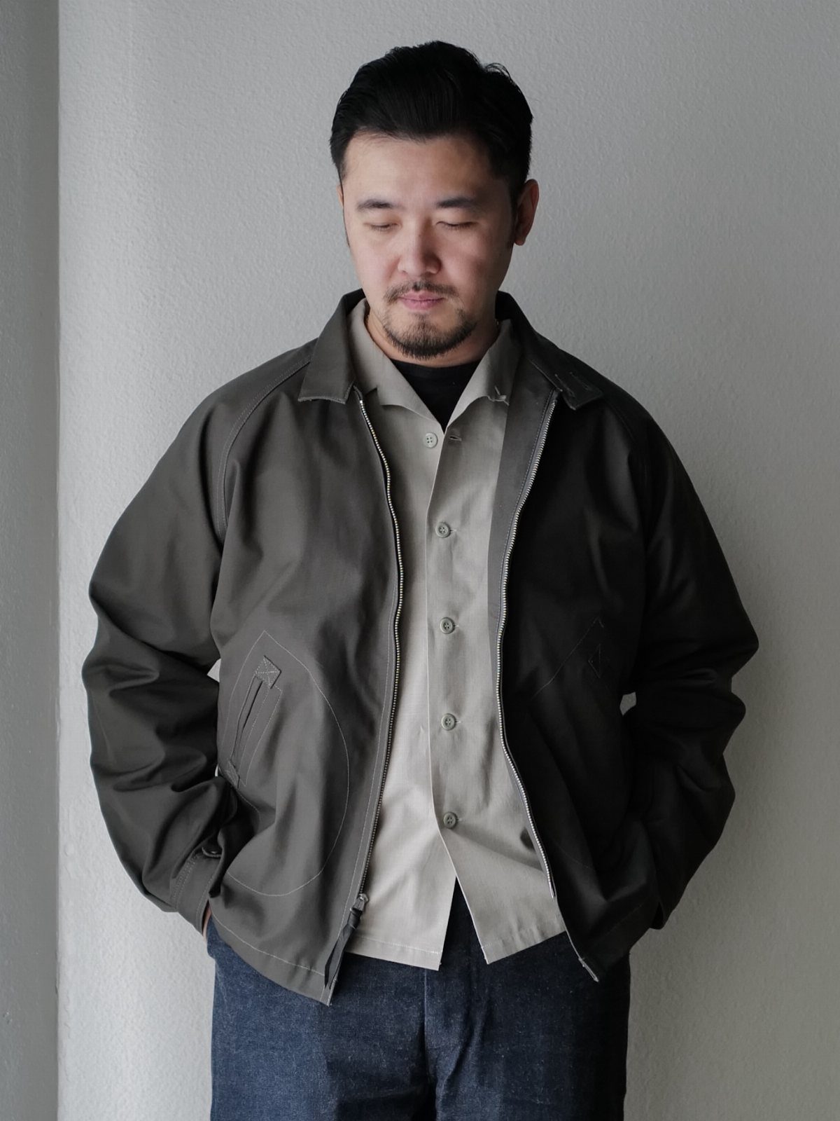 Man wearing a dark olive green minimalist jacket over a light grey button-down shirt.