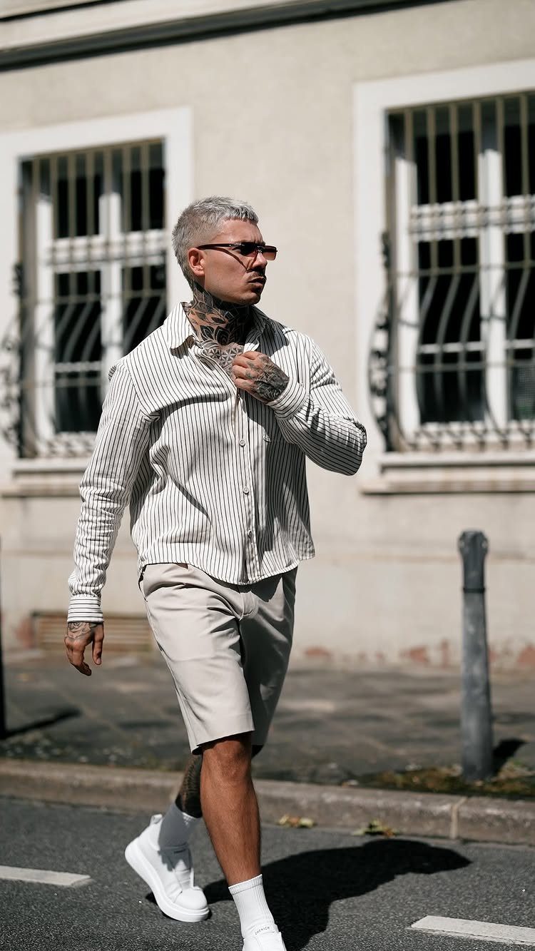 Man walking in a striped shirt and beige tailored shorts with white sneakers.