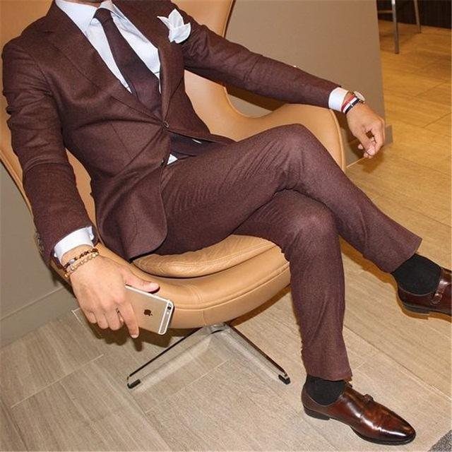 Man in a brown textured suit sitting in a tan leather chair holding a smartphone.
