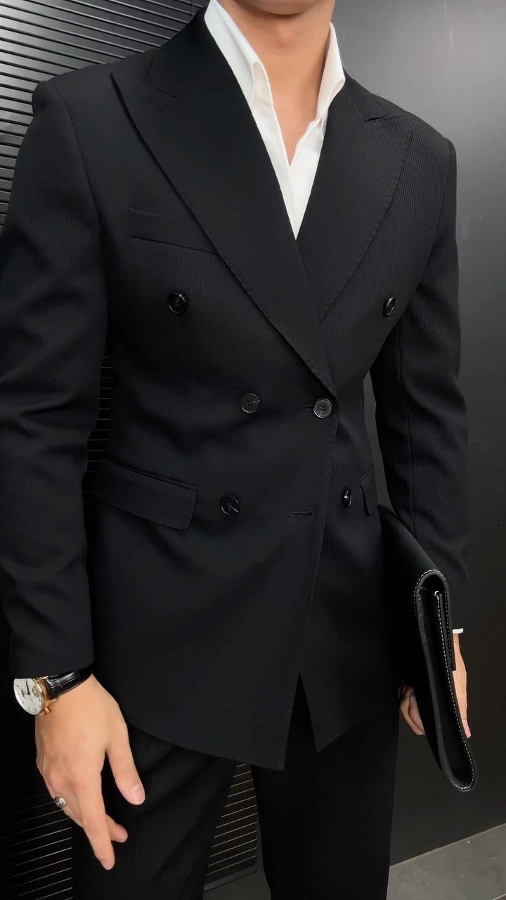 A man wearing a black double-breasted suit jacket and a white open-collar shirt.
