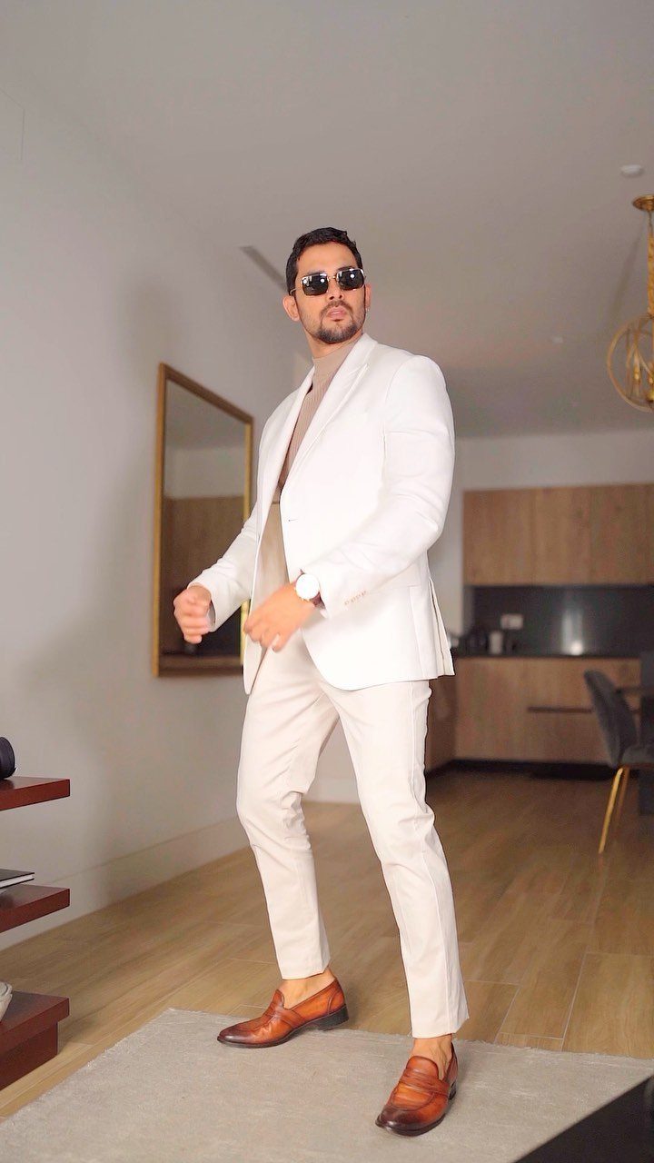 Man in a white slim-fit suit and brown loafers posing in a modern interior.