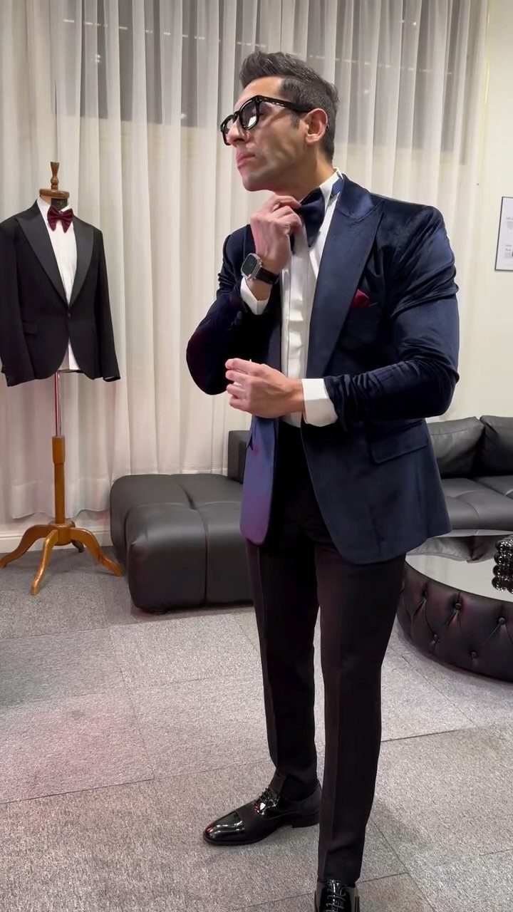 Man posing in a navy blue velvet tuxedo with a black bow tie and white shirt.