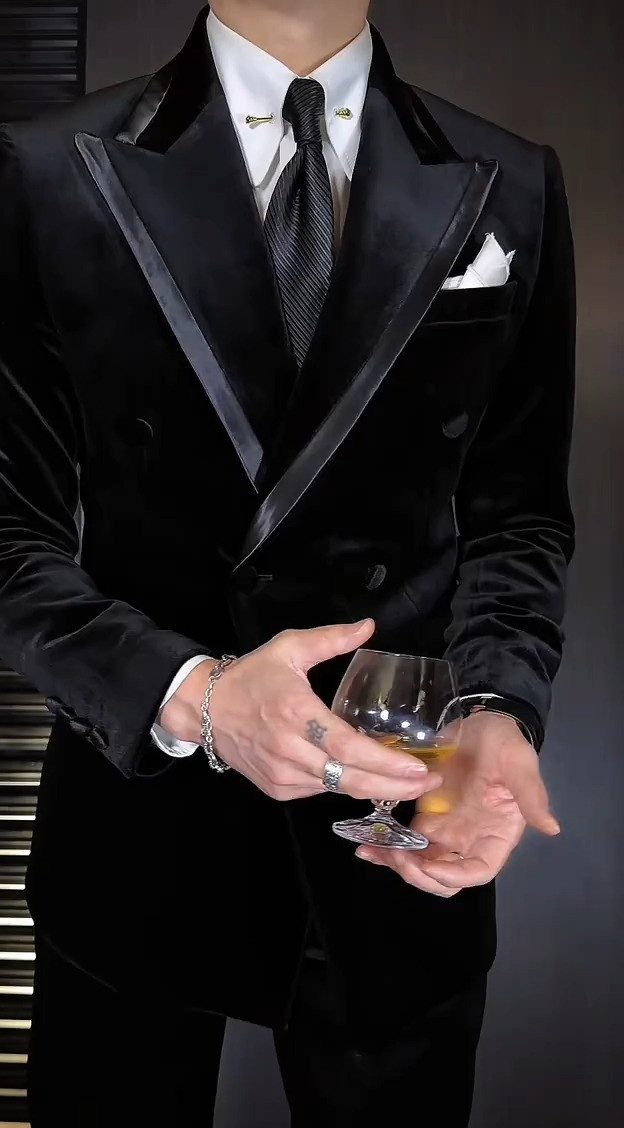 Man wearing a luxurious black velvet double-breasted suit jacket while holding a glass.