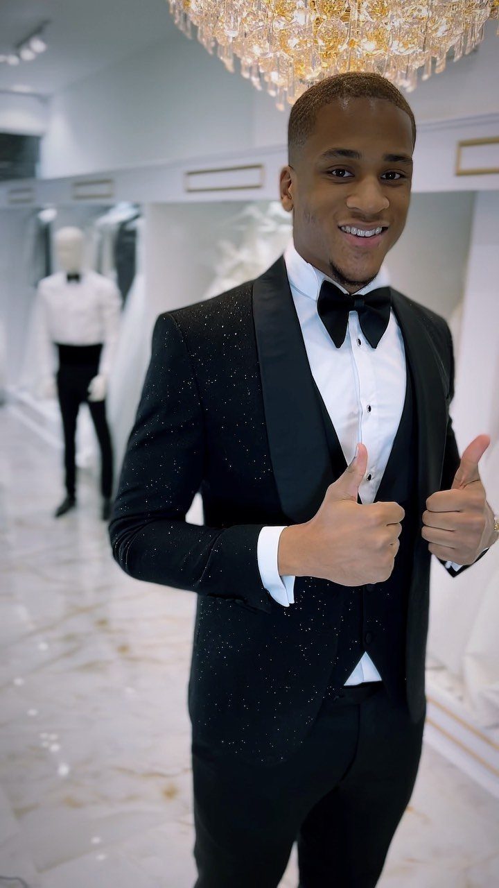 A smiling man in a black tuxedo and bow tie giving two thumbs up.