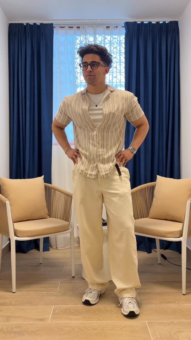 Man posing in a cream striped shirt, cream trousers, and white sneakers.