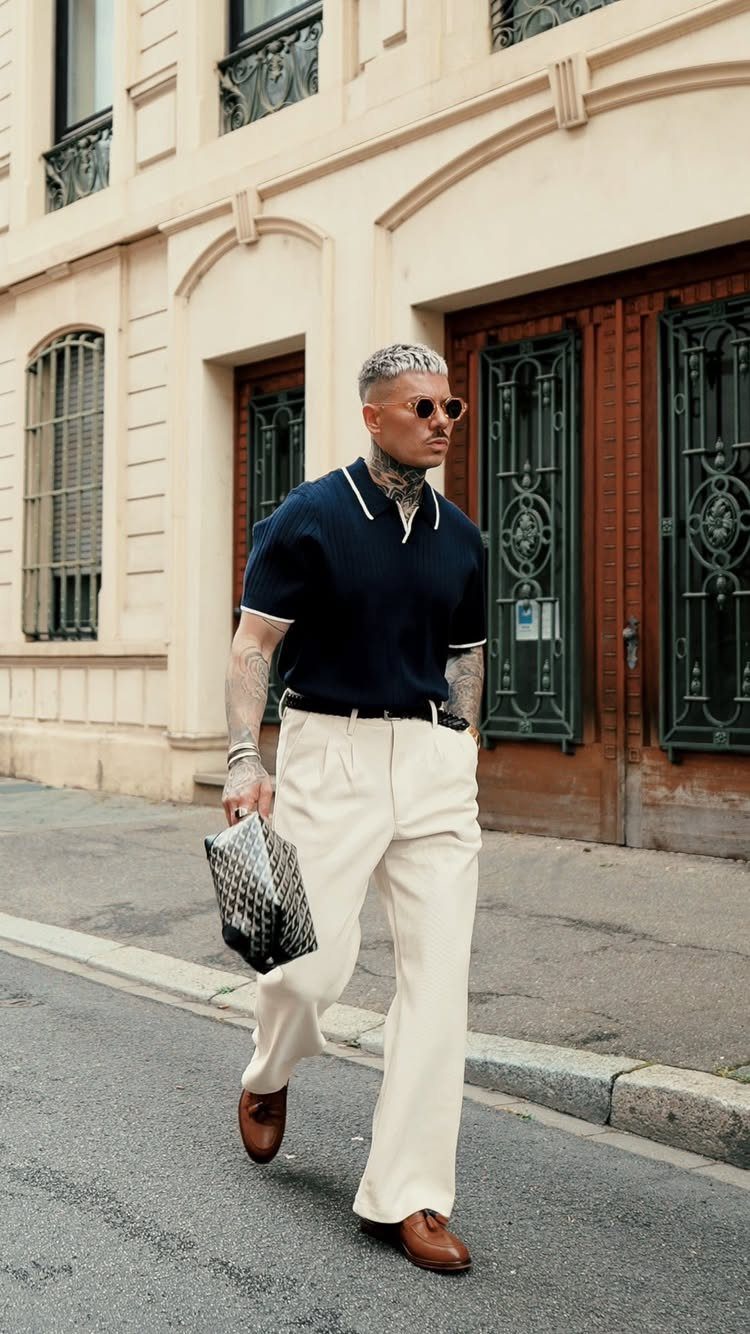 Man in navy short-sleeve polo and cream trousers walking down a city street.