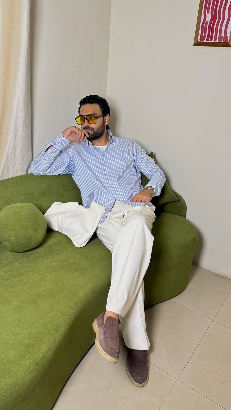 Man in striped shirt and white pants sitting on a green sofa wearing sunglasses.