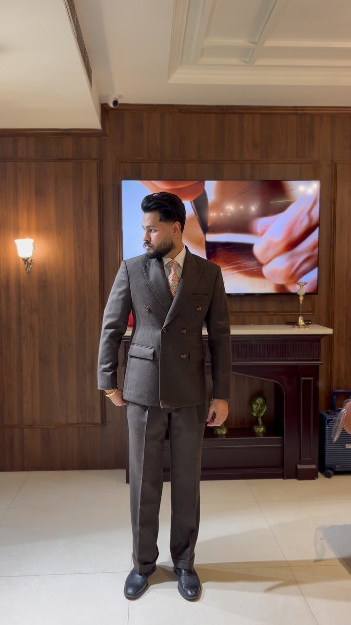 A man posing in a dark grey double-breasted suit and black dress shoes.