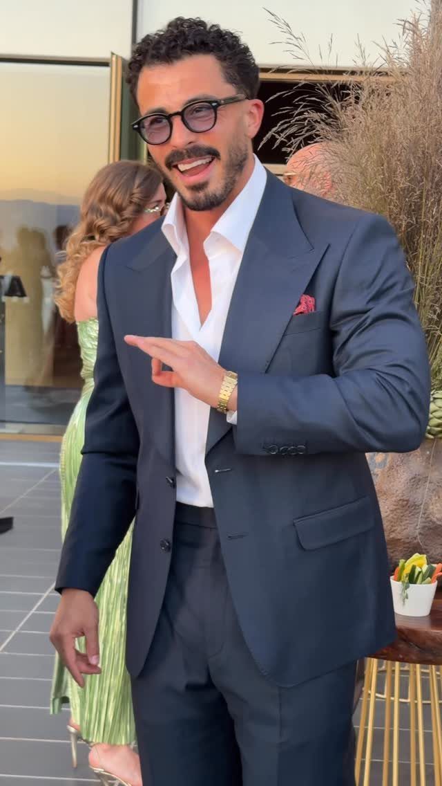 A smiling man in a navy blue suit and white shirt posing outdoors.