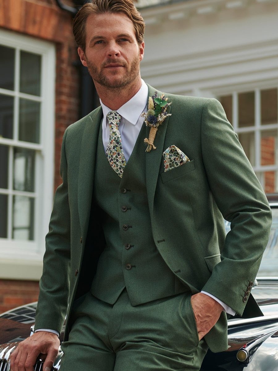 A man wearing a sage green three-piece suit with a floral tie and pocket square.