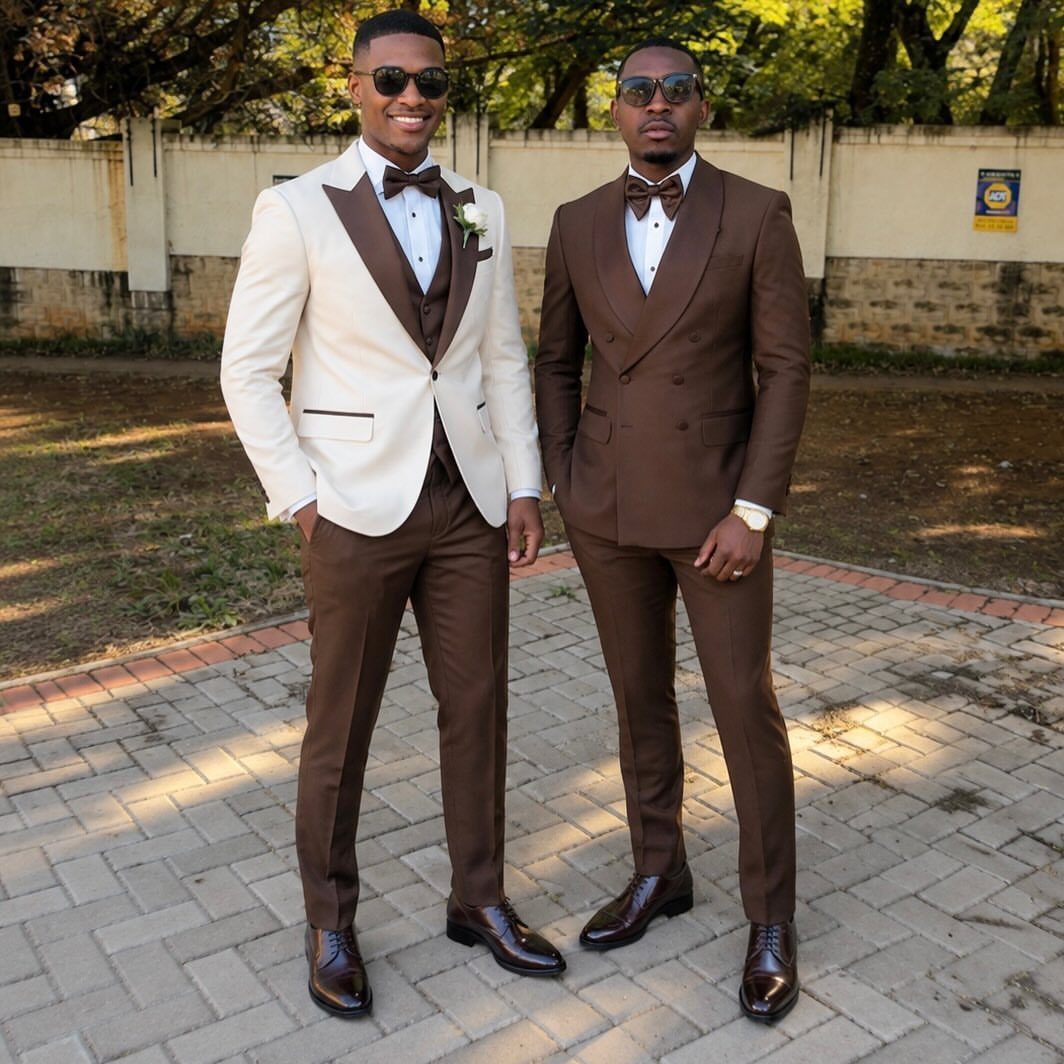 Two men posing in stylish cream and brown formal wedding suits and sunglasses.