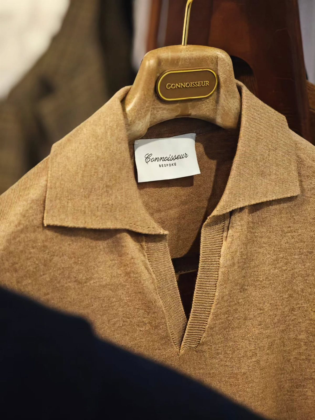 Tan knit polo shirt with a collar hanging on a wooden hanger in a shop.