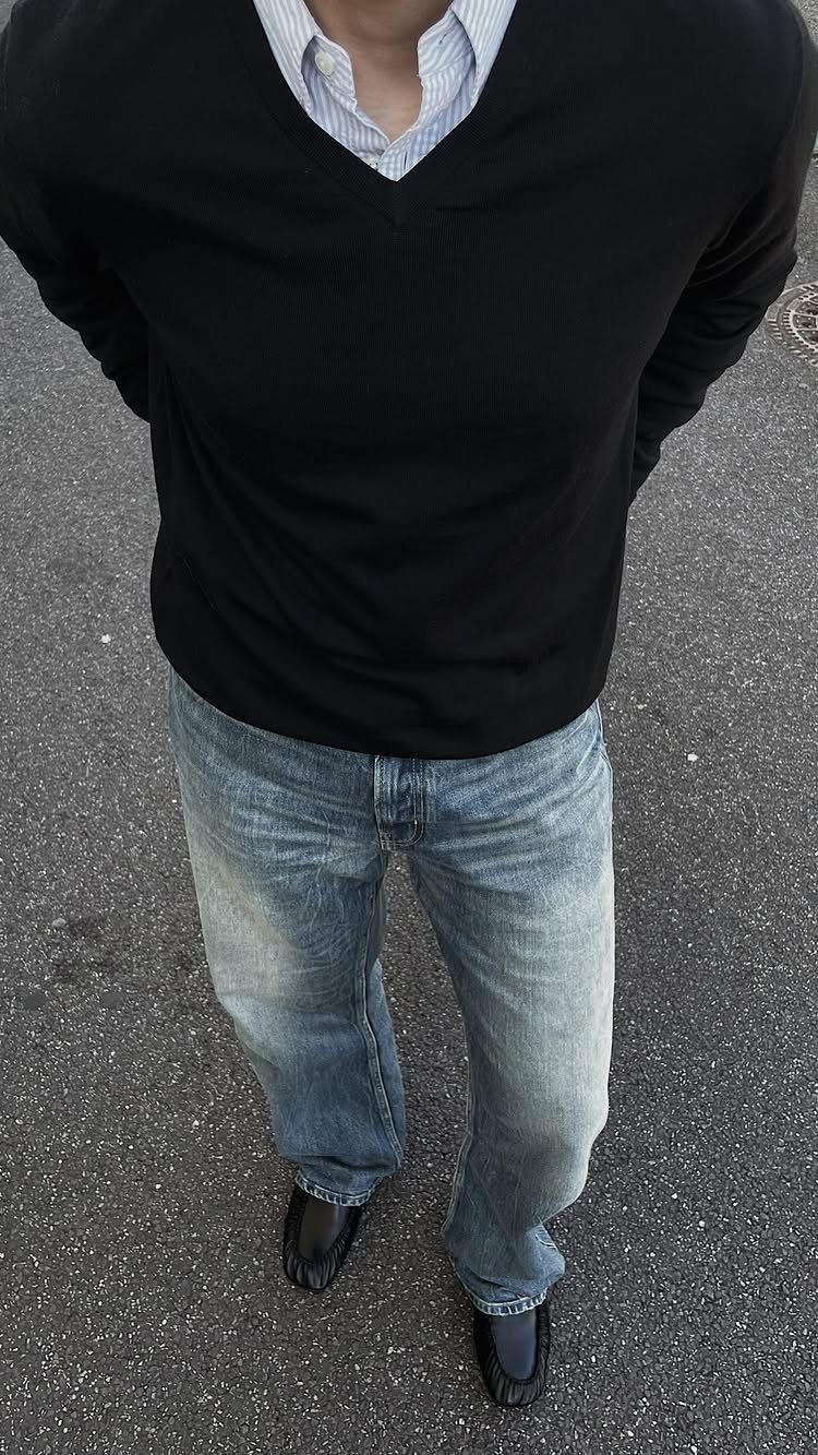 A person wearing a black v-neck sweater, striped shirt, and light blue denim jeans.