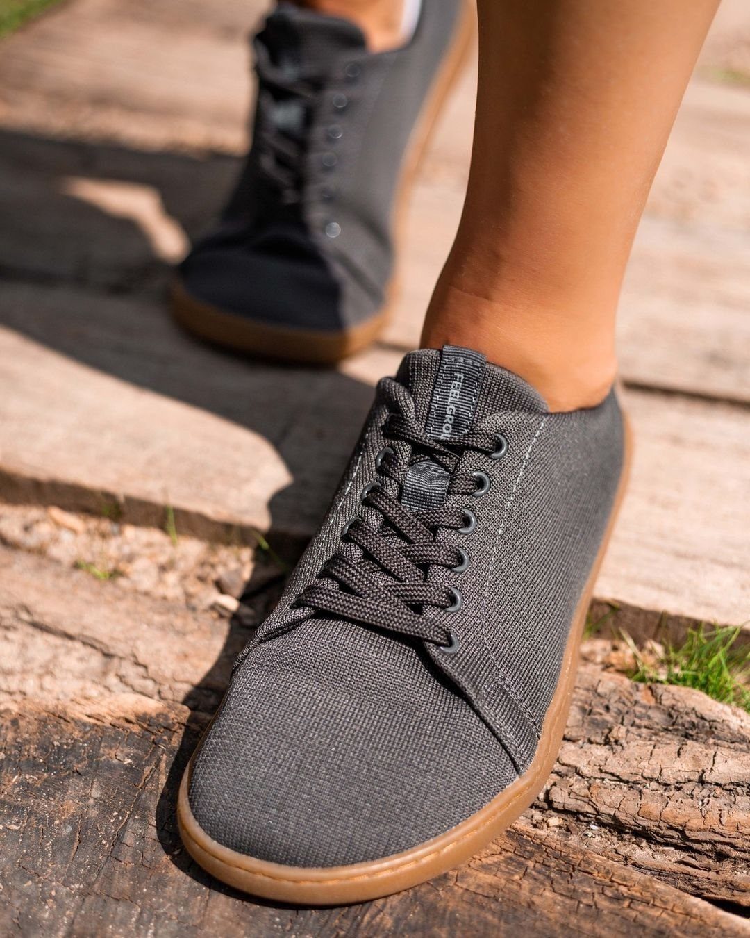 Grey canvas lace-up sneakers with tan soles being worn while walking on wooden planks.