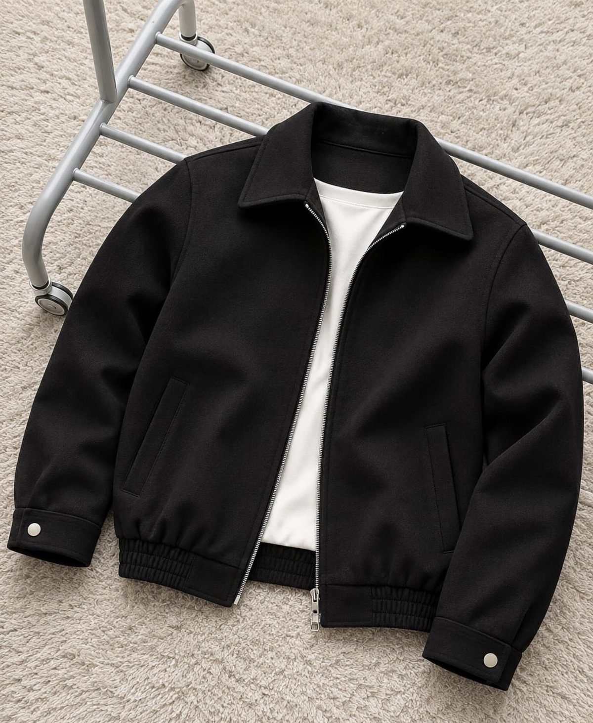 Black structured jacket with a silver zipper over a white t-shirt on a textured surface.