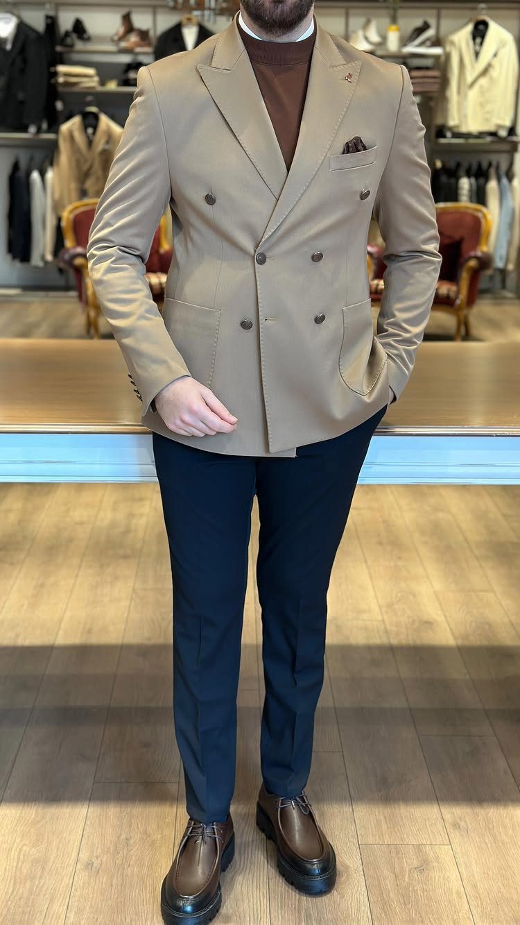 Man wearing a tan double-breasted blazer, brown turtleneck, navy trousers, and brown leather shoes.
