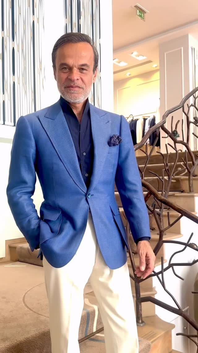 Man in a perfectly tailored blue blazer and cream trousers standing by a staircase.