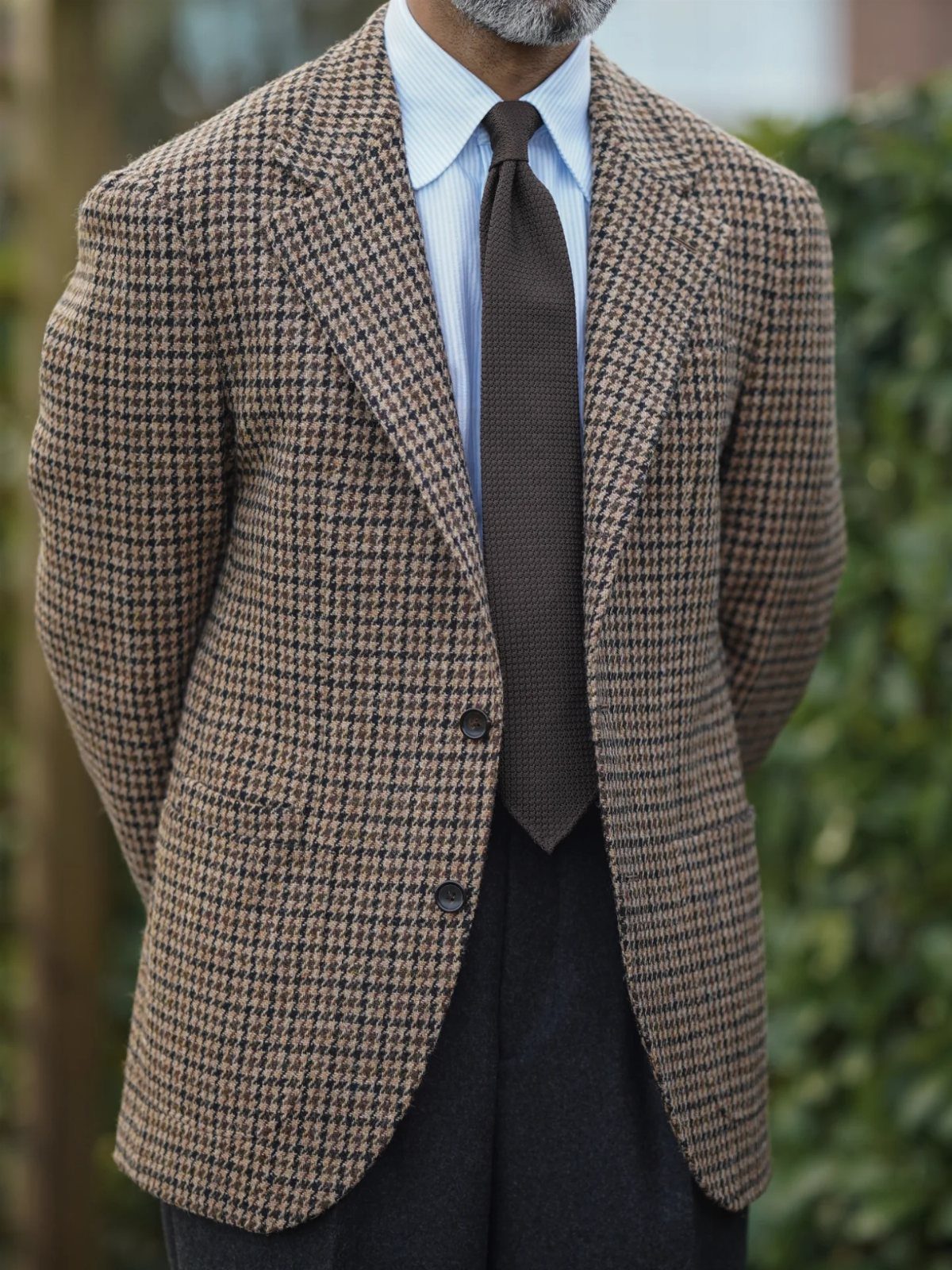Man wearing a brown and tan houndstooth pattern blazer with a blue shirt and brown tie.