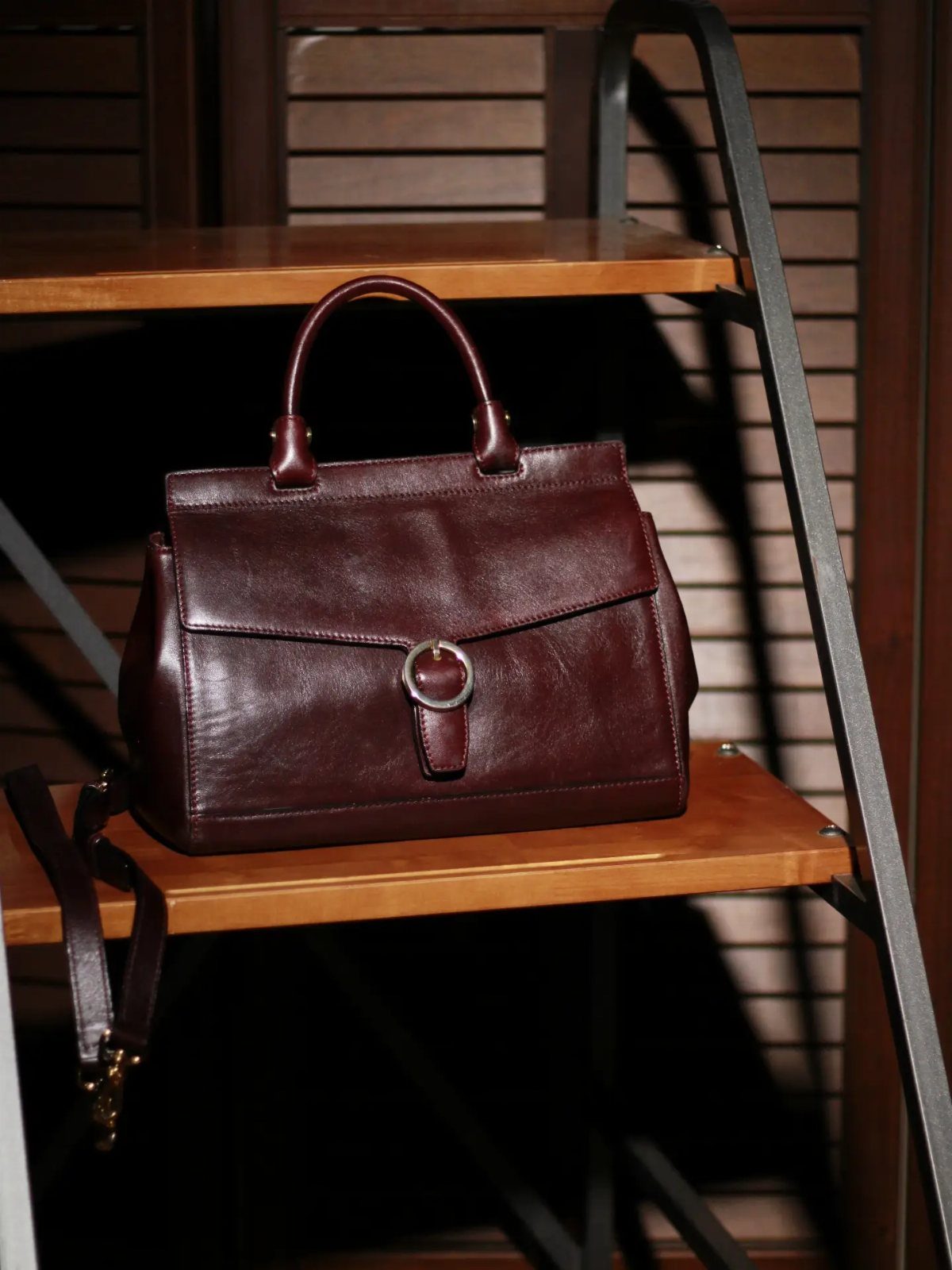 A burgundy leather handbag with a silver ring clasp resting on a wooden shelf.